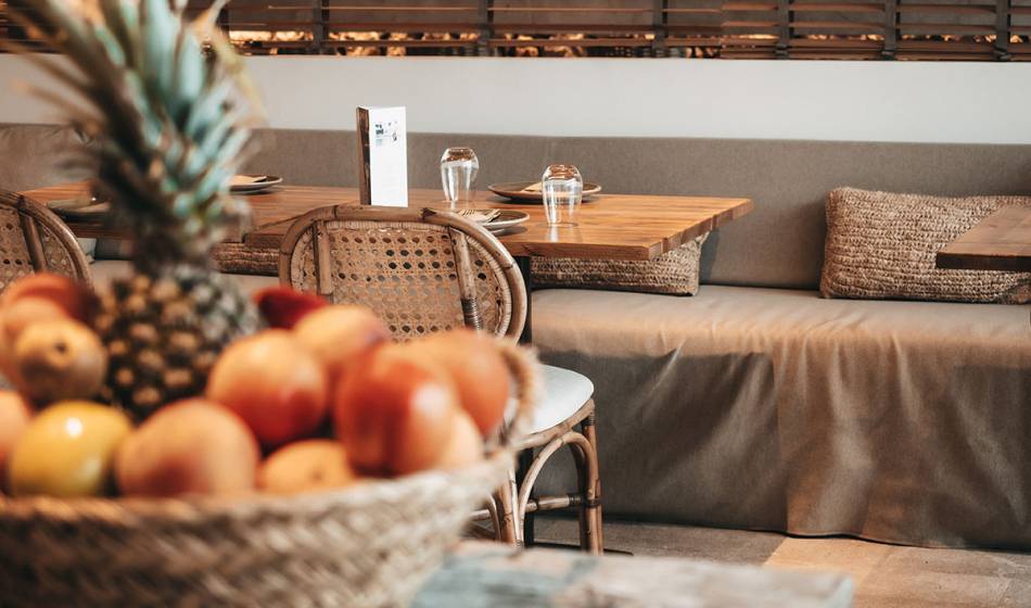 A basket of fresh fruit, including a pineapple and apples, stands on a table in the restaurant area of ​​the Barefoot Hotel Mallorca.