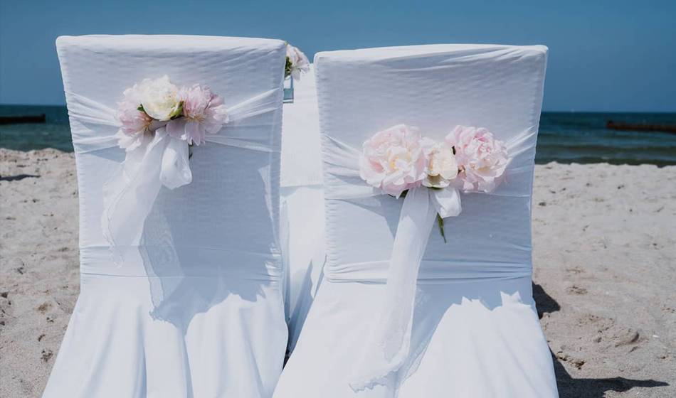 Wedding chairs on the beach with white covers and flower decorations, perfect for a wedding on the Baltic Sea.