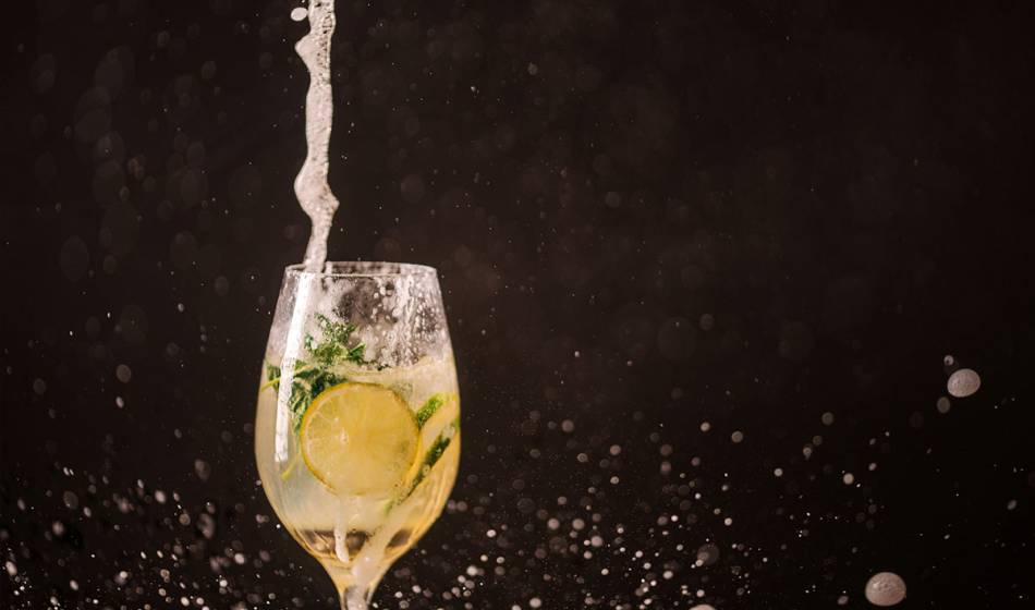 An aperitif glass with fizzy drink, lemon slice and fresh mint, against a black background.