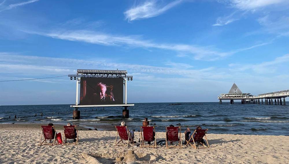 Sommerkino am Strand von Heringsdorf mit großer Leinwand im Wasser und Zuschauern im Sand vor der Ostsee.