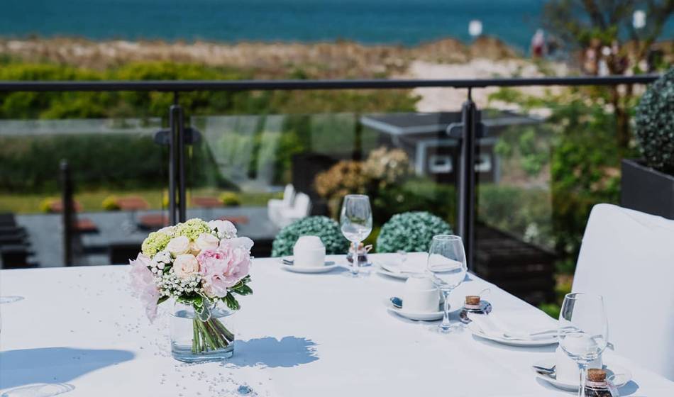 Festively laid table with flower arrangement and wine glasses, in the background the Baltic Sea in the Hotel Seezeichen.