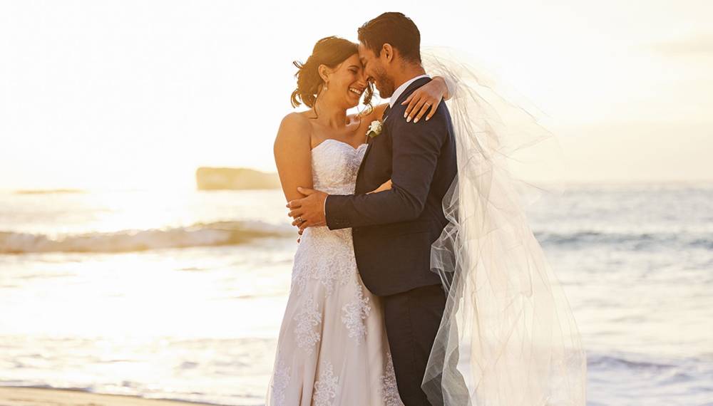 Hochzeitspaar steht am Strand auf Mallorca und genießt die Zeit zu zweit.