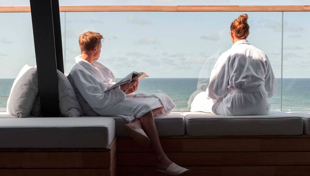 Ein Paar sitzt entspannt in der Spa.Lounge des Wyn. Strandhotels Sylt mit Blick auf die Nordsee.