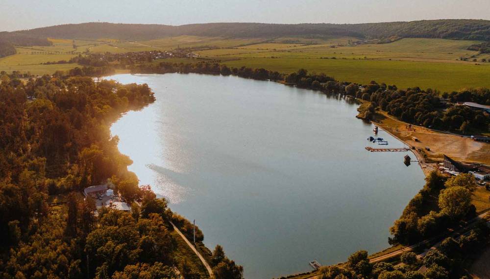 Porträt vom Stausee Hohenfelden in Thüringen mit Badebereich, Wiesen, Stegen und bewaldeten Ufern im Sonnenlicht