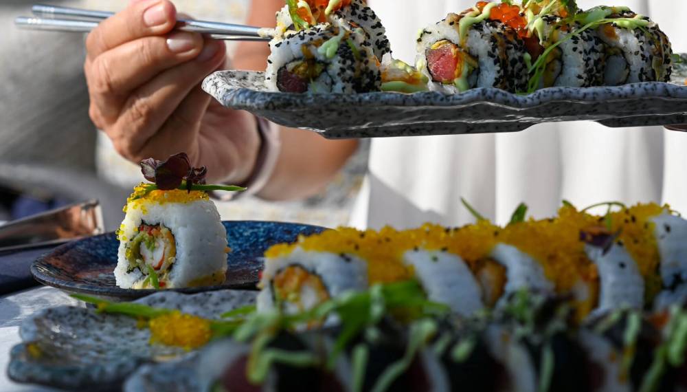 Eine Person hält Stäbchen in der Hand und hat vor sich Sushi-Rollen auf einem Teller.
