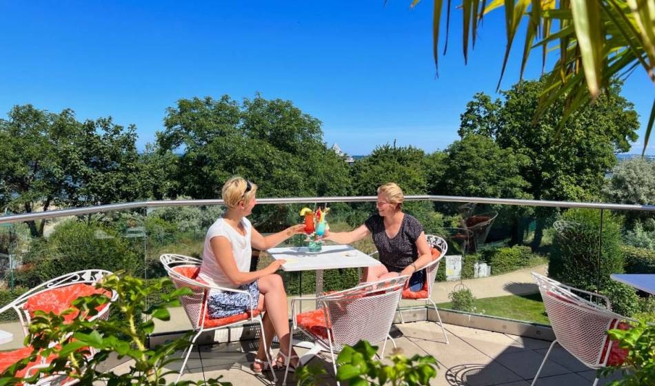 Zwei Frauen genießen Cocktails auf der Terrasse des Kaiserhof Heringsdorf auf Usedom mit Blick auf die Ostsee und sommerlicher Atmosphäre.