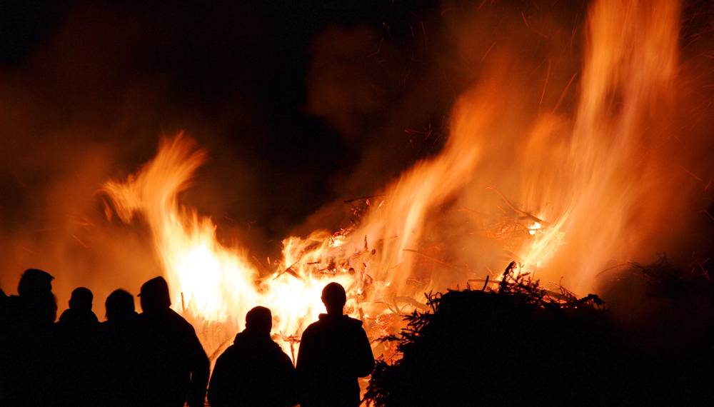 Eine Gruppe von Menschen steht in der Walpurgisnacht vor einem großen Maifeuer.