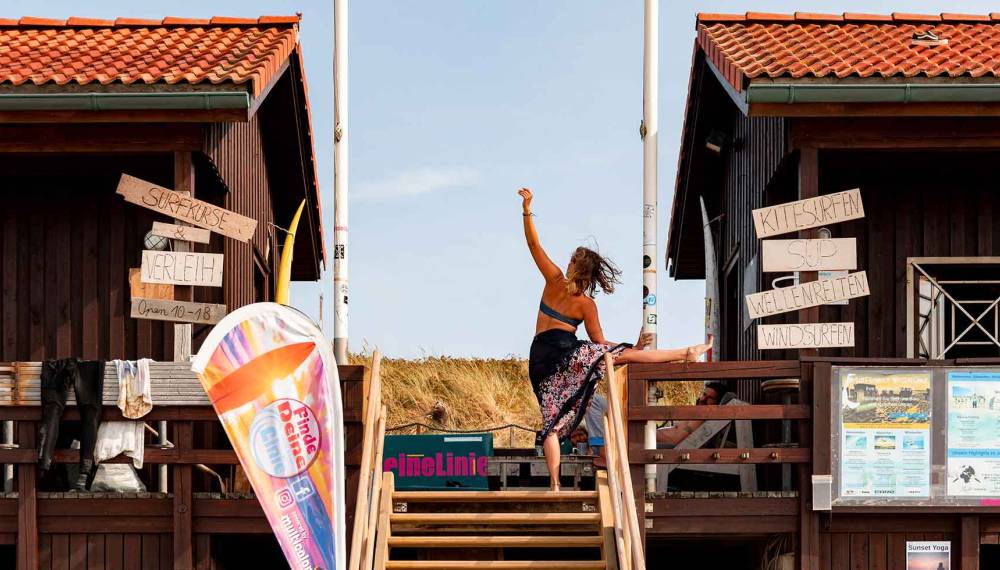 Frau macht Yoga auf der Treppe einer Surfschule auf Sylt.