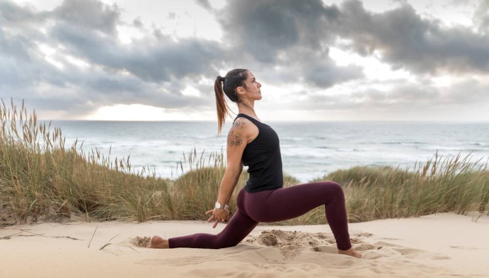 Halima Elkasmi praktiziert Yoga in einer tiefen Dehnpose auf einer Sanddüne beim Yoga Retreat im Vju Hotel auf Rügen.