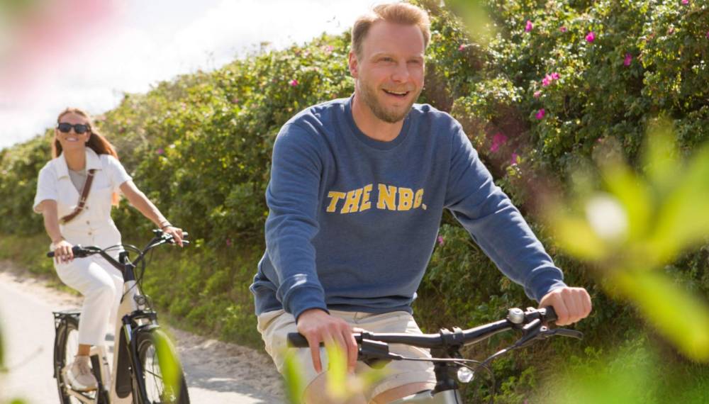 Fahrradtour auf Sylt: Zwei Personen radeln entspannt durch eine grüne, sonnige Dünenlandschaft.