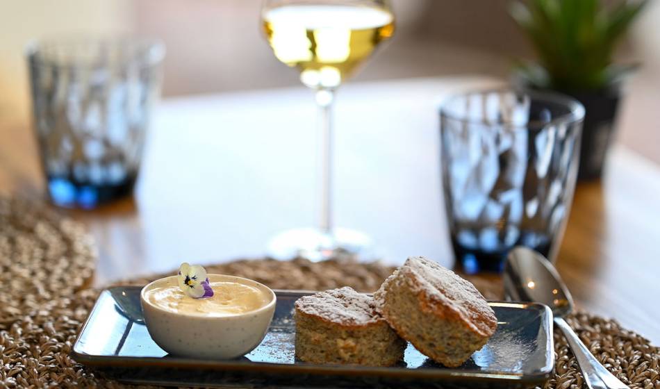 Two pieces of pastry with a dip on a black plate, served with a glass of white wine at the Barefoot Hotel Mallorca.