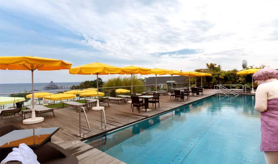 Outdoor pool at Kaiserhof Usedom, surrounded by loungers and parasols, with the Baltic Sea in the background.