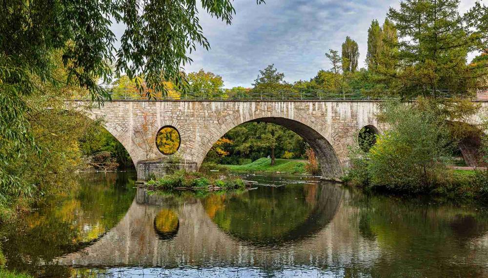 Historische Steinbrücke im Park an der Ilm in Weimar mit Spiegelung im Wasser.