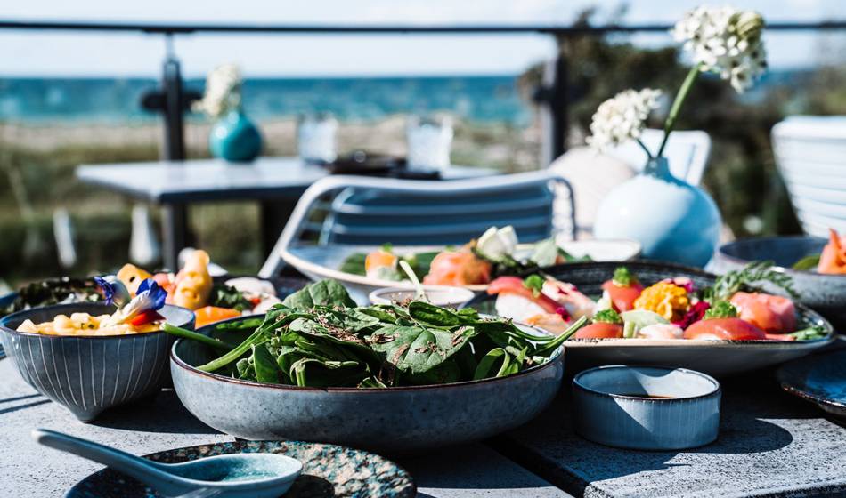 Various plates of fresh food such as salad, sushi and dips on the terrace with a sea view at #herrhoshi.