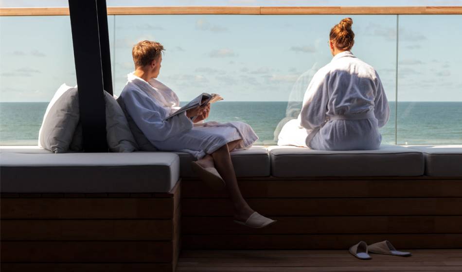 Zwei Personen in Bademänteln genießen den Meerblick auf der Terrasse des Wellnessbereichs im Wyn auf Sylt.