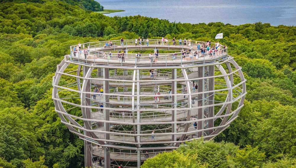 Baumwipfelpfad auf Rügen in Kugelform aus Holz, führt spiralförmig durch grüne Baumkronen mit vielen Besuchern.