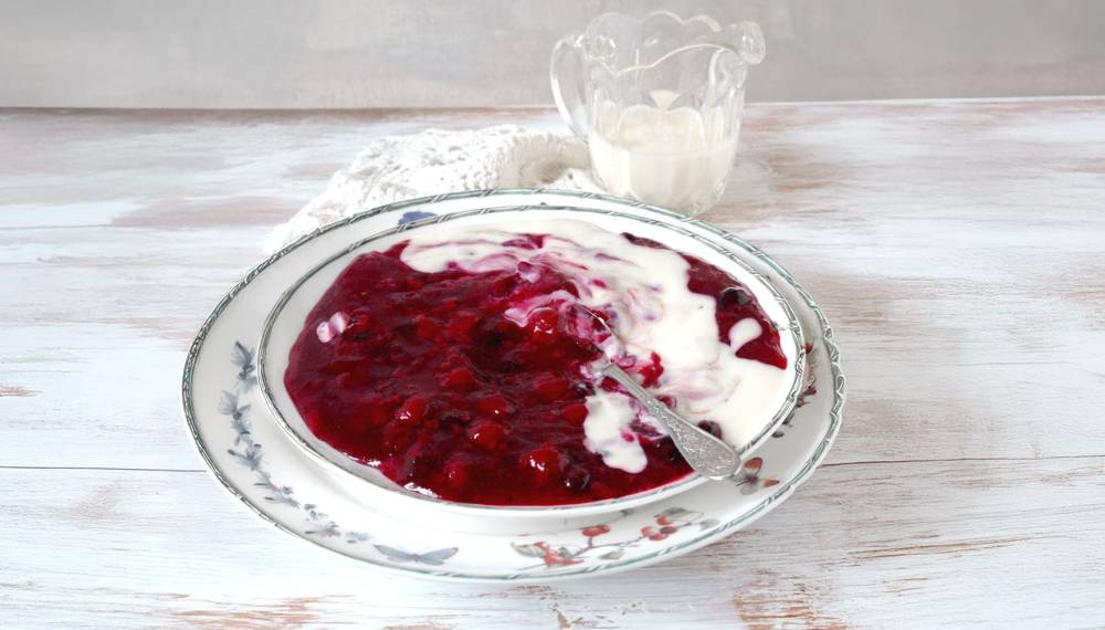 Rote Grütze mit Vanillesauce in einer Schale, dekoriert mit frischen Beeren und einem Minzblatt, eine wahre Rügener Spezialität.
