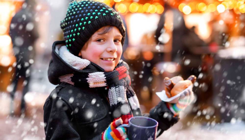 Kind mit Thüringer Rostbratwurst und heißer Schokolade auf dem Weihnachtsmarkt.