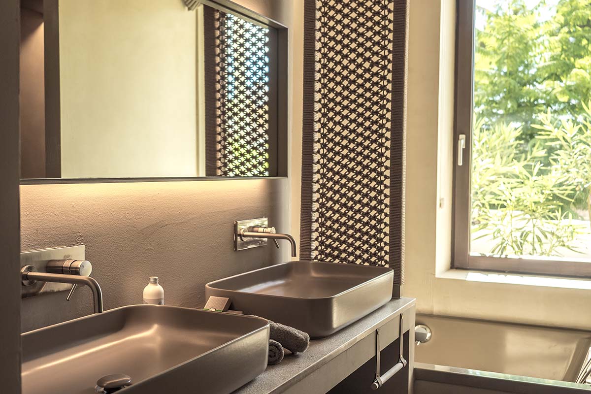 Modernes Badezimmer in der Suite Patio des Barefoot Hotel Mallorca mit zwei Waschbecken, großen Spiegeln und Blick ins Grüne