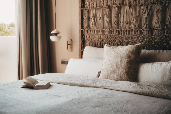 Gemütliches Bett mit dekorativem Kopfteil, Kissen und einem Buch in der Lado Campo Suite im Barefoot Hotel auf Mallorca.