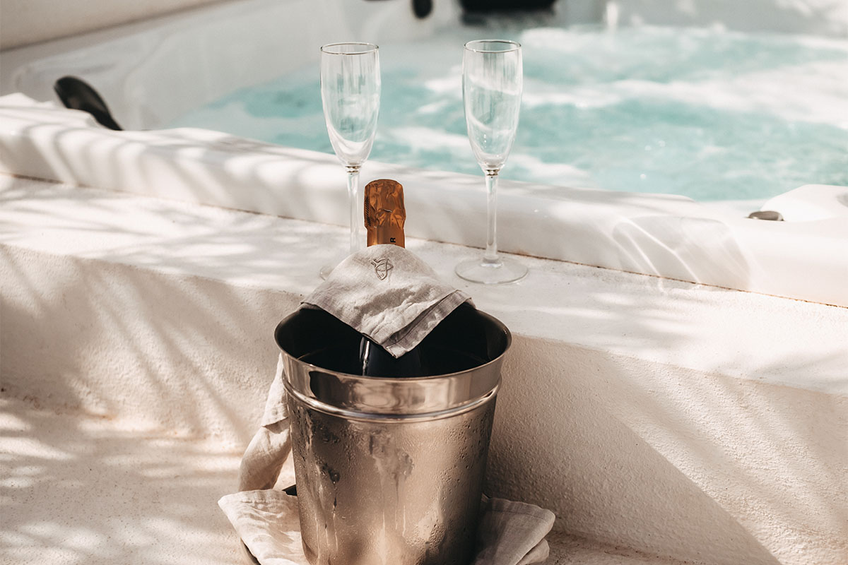 Ein Eiskübel mit Champagnerflasche und zwei Gläsern am Whirlpool, eingerahmt von Sonnenlicht in der Campo Lado Suite im Barefoot Hotel.