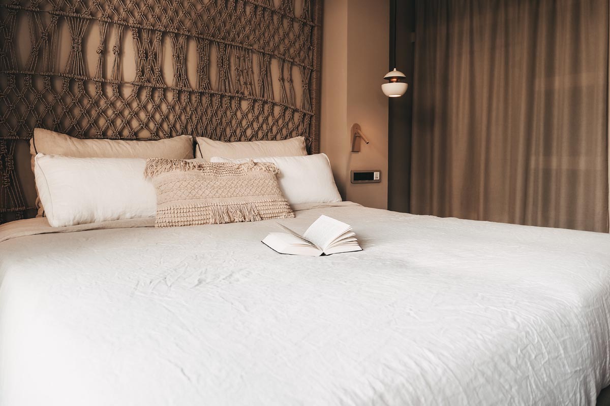 Bequemes Doppelbett im  Doppelzimmer Puerto des Barefoot Hotel Mallorca mit dekorativem Kopfteil und offenem Buch
