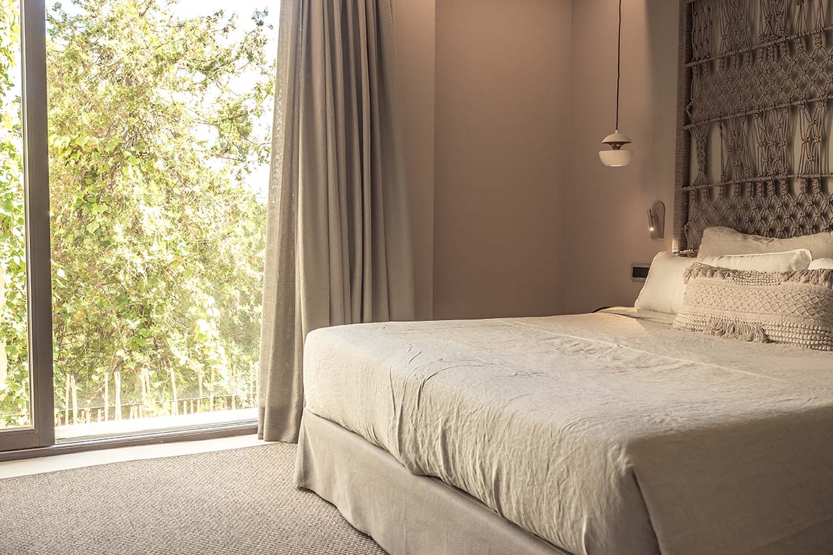 Hotelzimmer Puro mit einem großen, gemütlichen Bett und Blick auf grüne Bäume im Barefoot Hotel Mallorca.