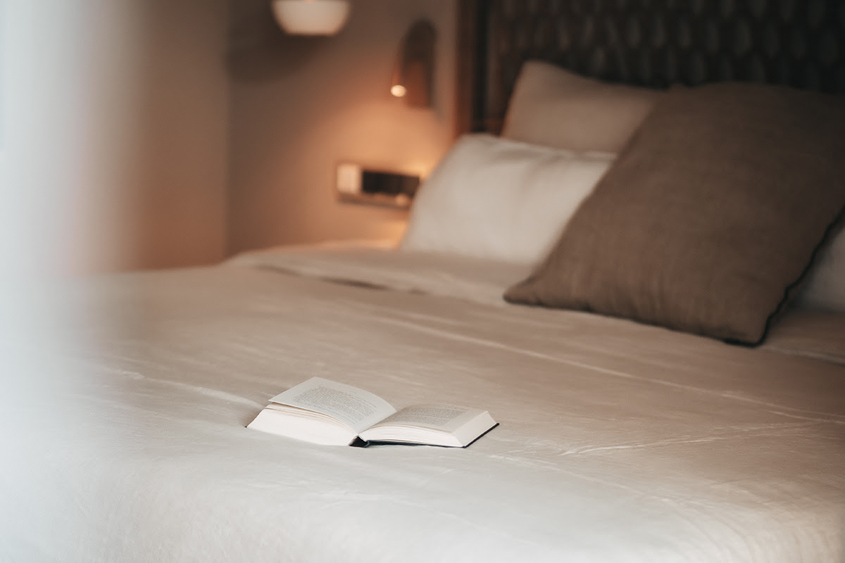 Zona de descanso en la habitación Pino del Hotel Barefoot Mallorca con un libro abierto sobre una gran cama y acogedoras almohadas.