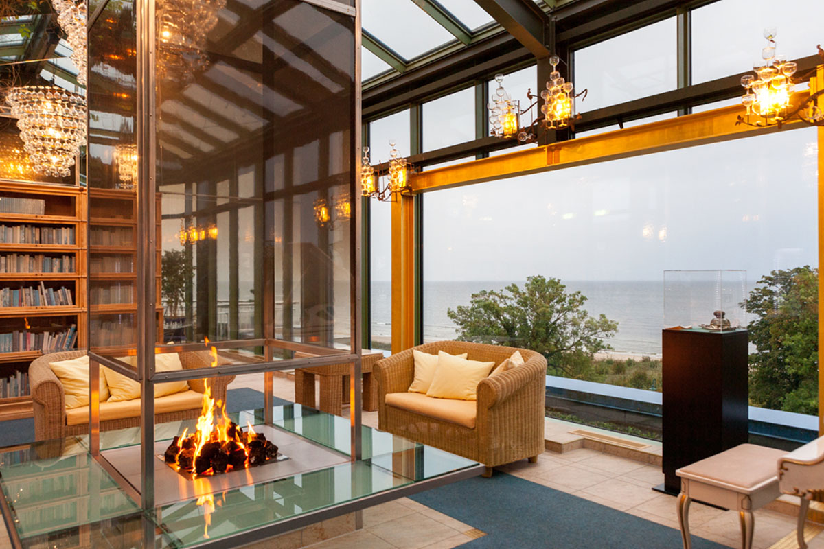 Wintergarten im Hotel Kaiserhof Heringsdorf mit gemütlichen Sesseln, Kaminfeuer, Bücherregalen und Panoramablick auf die Ostsee.