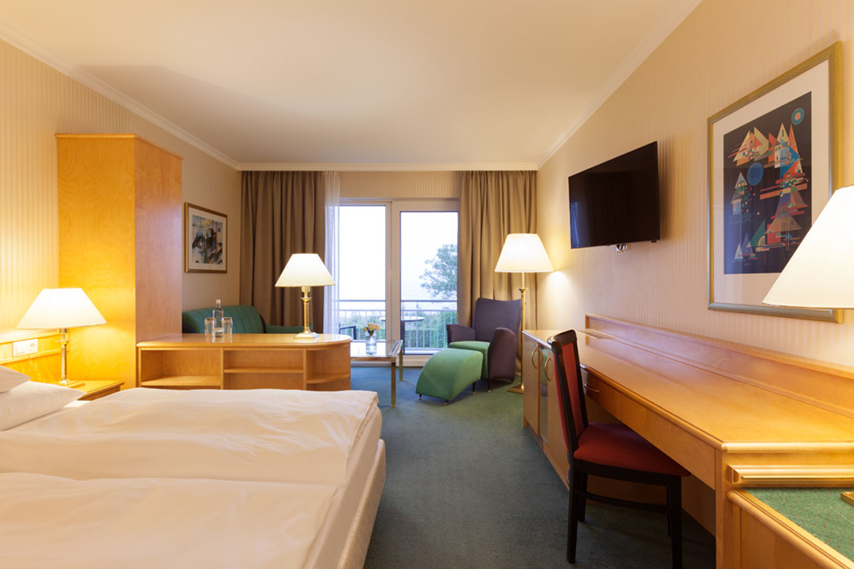 Hotelzimmer im Hotel Kaiserhof Heringsdorf mit Doppelbett, Schreibtisch, Sitzbereich, TV und Zugang zum Balkon mit Meerblick.