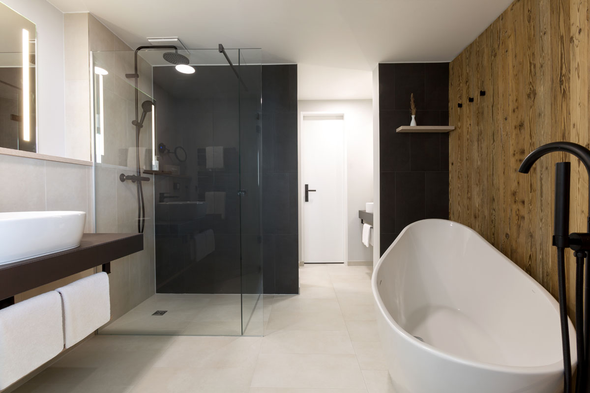 Bathroom of the Kaisersuite with free-standing bathtub, rainforest shower and stylish wood paneling in the Hotel Kaiserhof.
