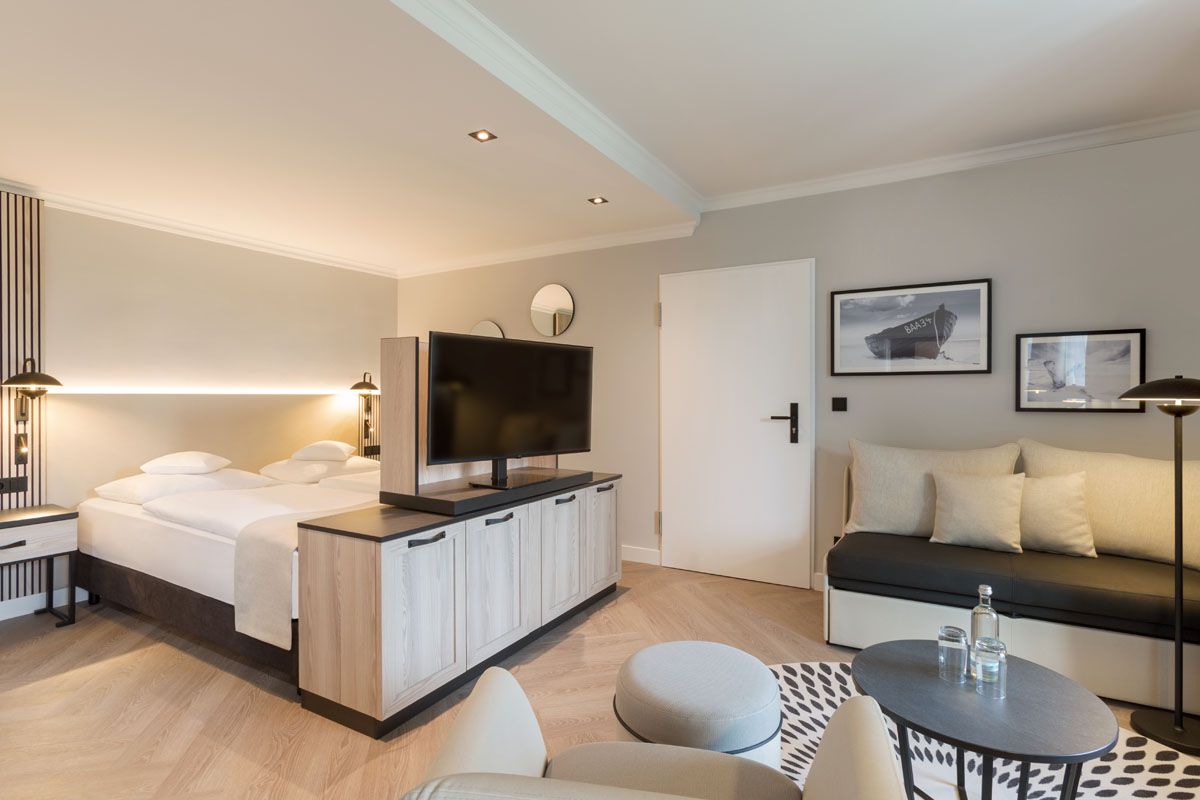 Overview of the themed suite with double bed, TV and seating area in a modern design at the Hotel Kaiserhof Heringsdorf.