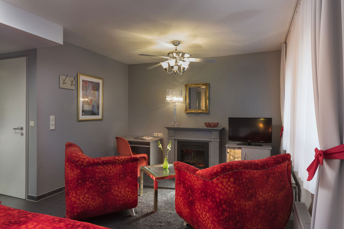 Seating area in the family room with two red armchairs, fireplace and mirror for a cozy family vacation at the Hotel Kaiserhof.