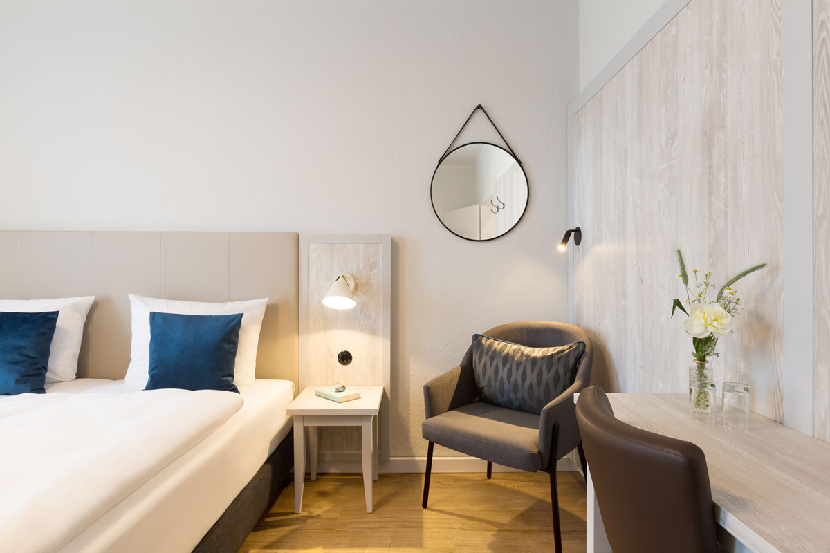 Einladendes Doppelzimmer im Koopmanns Hotel mit stilvoller Einrichtung, Sessel und dekorativem Spiegel an der Wand.