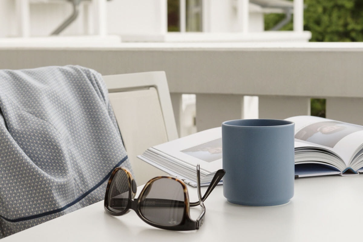 Detailaufnahme einer Tasse Kaffee, Sonnenbrille und Buch auf dem Balkon im Koopmanns Hotel &amp; Lädchen auf Rügen.
