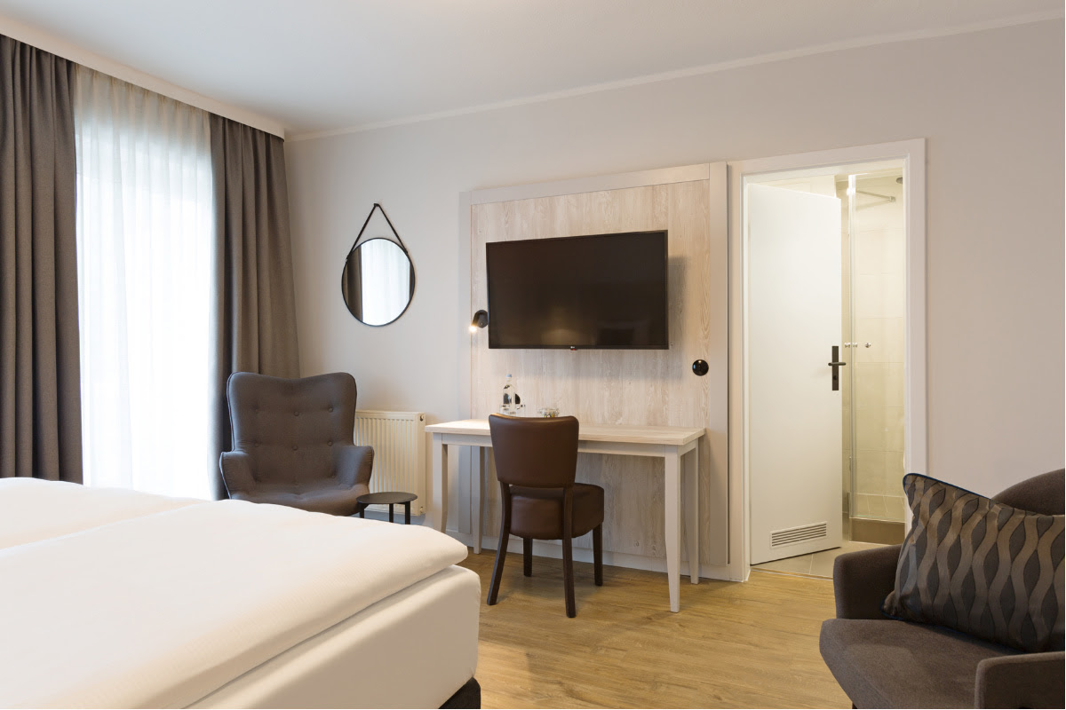 Modern eingerichteter Wohnbereich mit TV, Schreibtisch und Sitzgelegenheit im Doppelzimmer im Koopmanns Hotel.