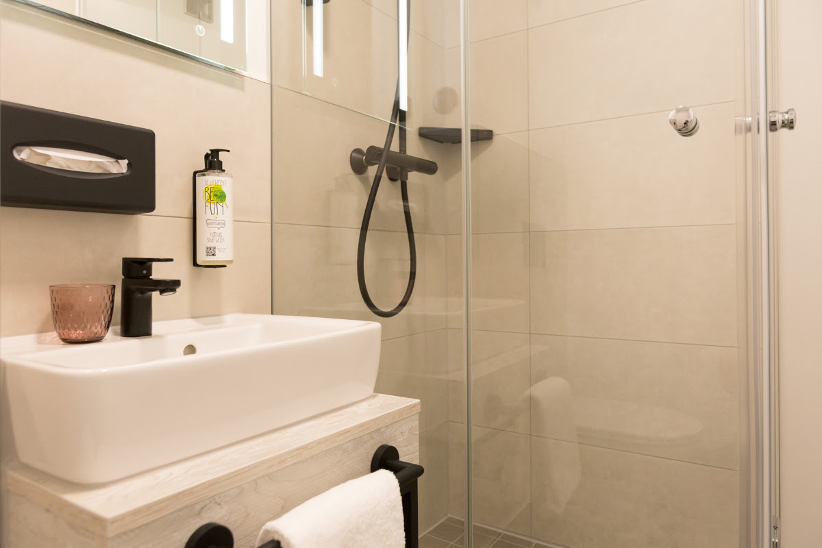 Helles Badezimmer mit Dusche, Waschbecken und moderner Ausstattung im Einzelzimmer des Koopmanns Hotel.