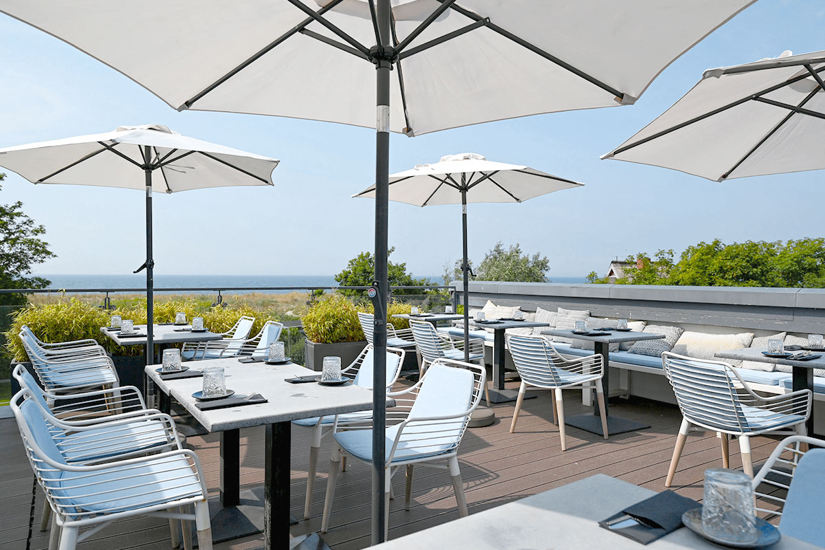 Elegante Restaurantterrasse im Künstlerquartier Seezeichen Ahrenshoop mit weißen Sonnenschirmen und Blick auf die Ostsee