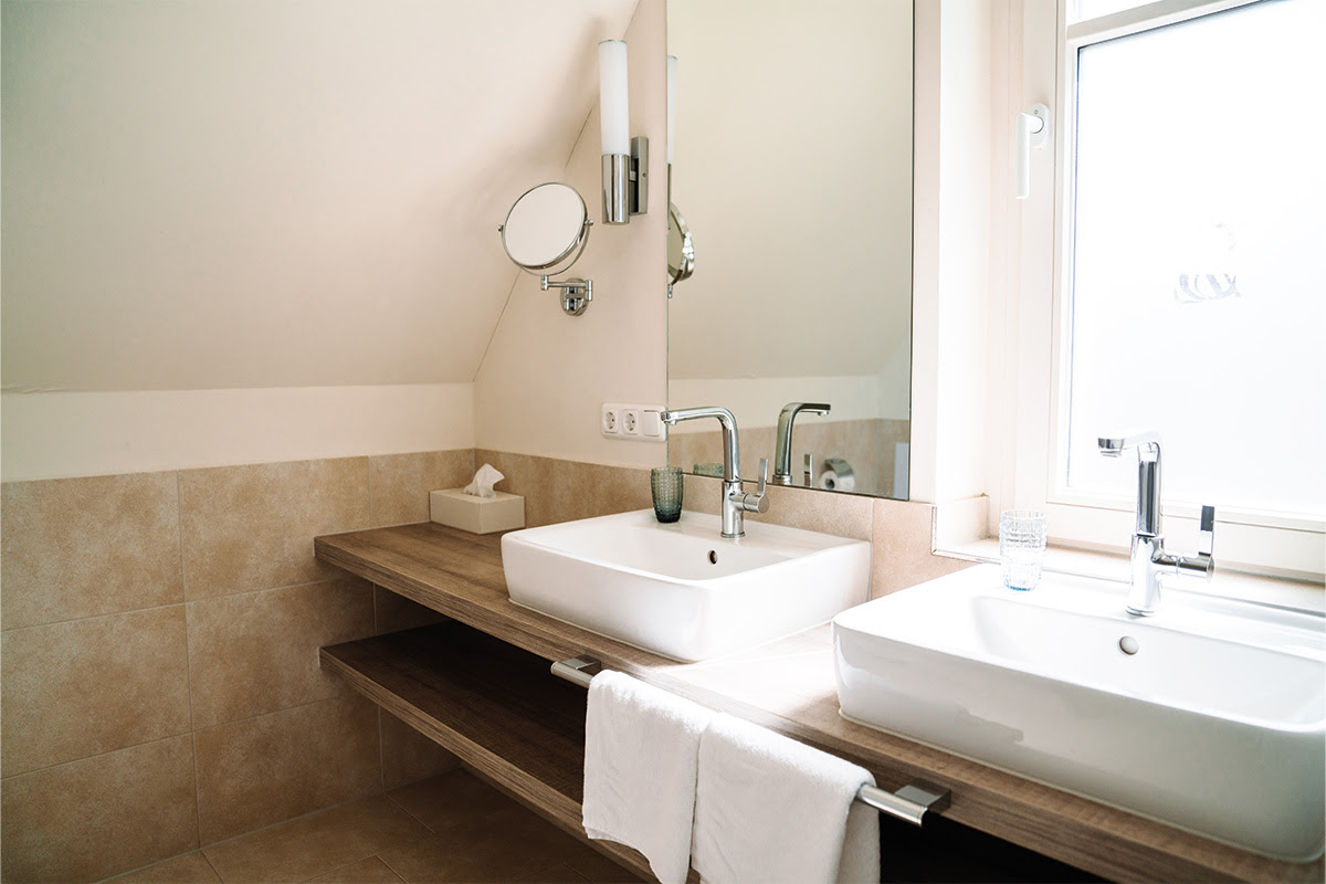Helles Badezimmer der Ferienwohnung Dünenpark in Hotel Künstlerquartier Seezeichen mit Doppelwaschbecken und Tageslicht.