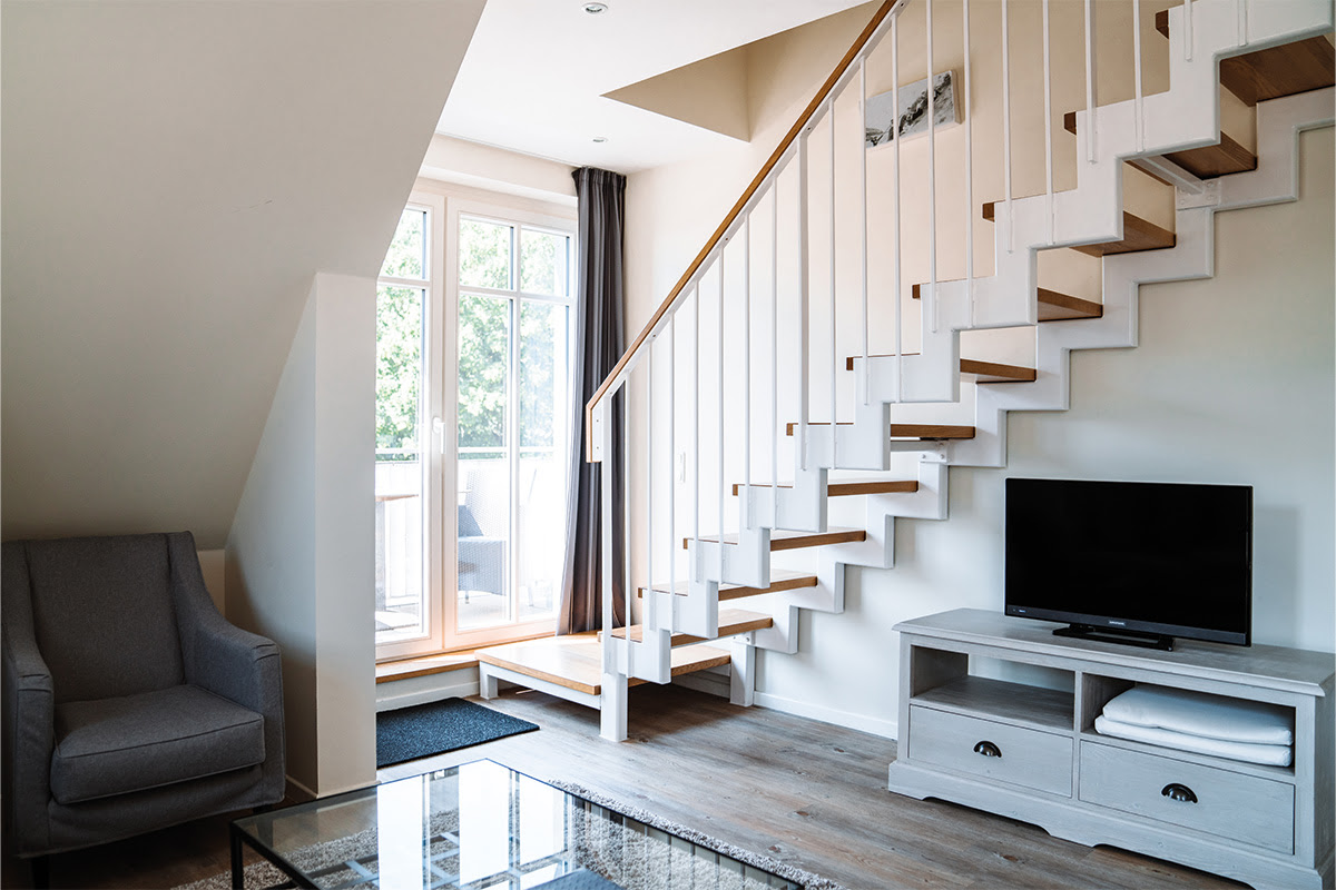 Wohnbereich der Ferienwohnung Dünenpark mit TV, gemütlichem Sessel und Treppe, als Teil des Hotel Künstlerquartier Seezeichen.