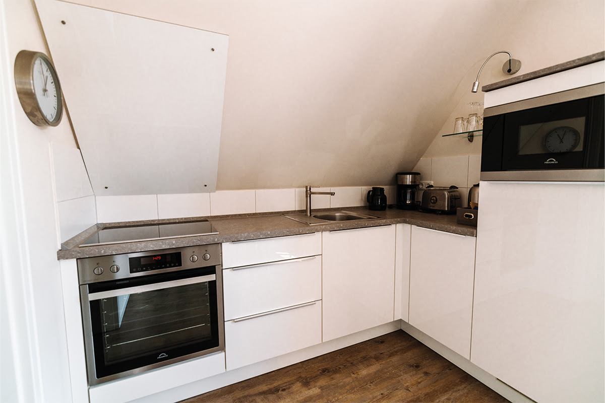 Moderne Küchenzeile der Ferienwohnung Seepferd im Dünenpark in Ahrenshoop mit Herd, Mikrowelle und Kaffeemaschine.