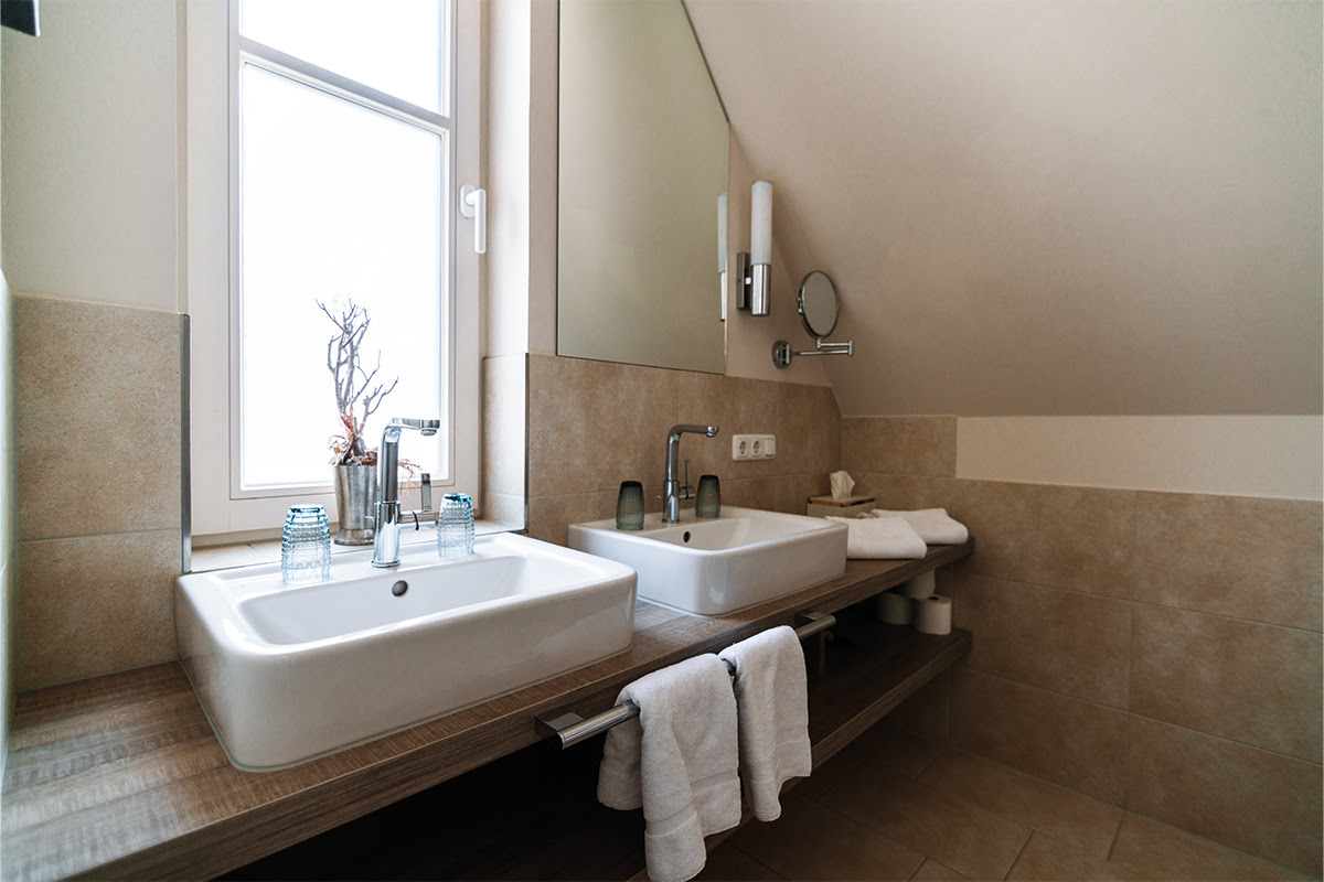 Badezimmer mit Doppelwaschbecken, modernen Armaturen und Spiegel in der Ferienwohnung Stranddüne im Dünenpark Ahrenshoop.