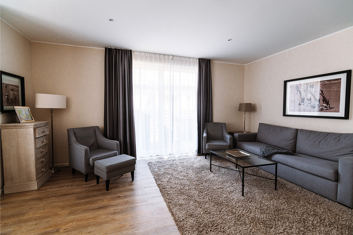 Komfortables Wohnzimmer mit großem Fenster und Sofa in der Ferienwohnung Strandmuschel im Hotel Künstlerquartier Seezeichen.
