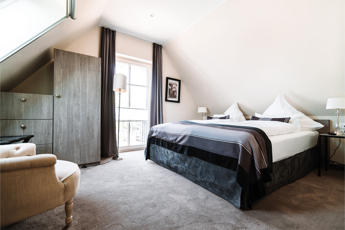 Schlafzimmer der Ferienwohnung Strandnixe mit Doppelbett, TV und viel Tageslicht, Teil des Hotels Künstlerquartier Seezeichen.