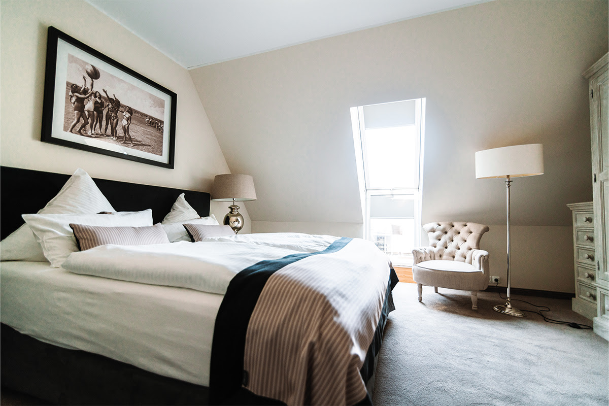 Schlafzimmer mit Doppelbett, Sessel und Dachschräge in der Ferienwohnung Strandperle im Hotel Künstlerquartier Seezeichen.