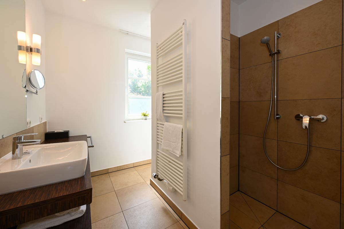 Modernes Badezimmer mit ebenerdiger Dusche, Waschbecken und Handtuchheizung in der Ferienwohnung Seeadler in Ahrenshoop.