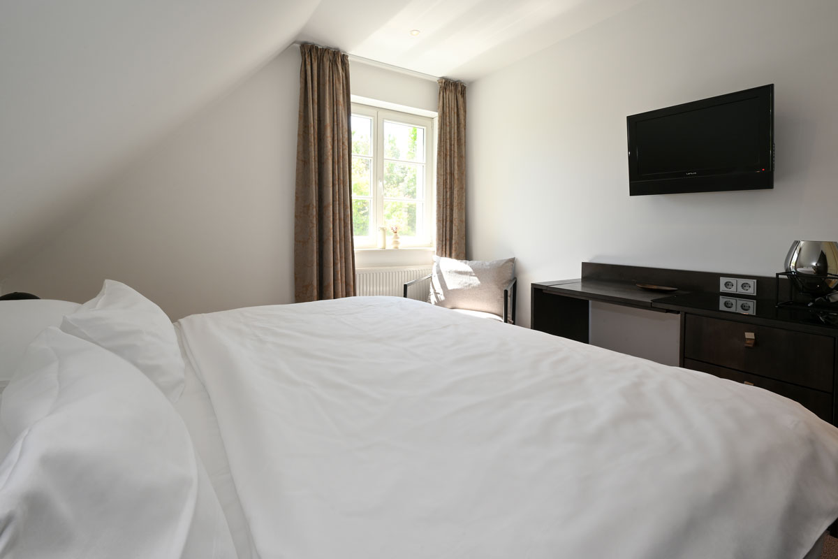 Gemütliches Schlafzimmer mit Doppelbett und hellem Fenster in der Ferienwohnung Seeadler im Hotel Künstlerquartier Seezeichen.