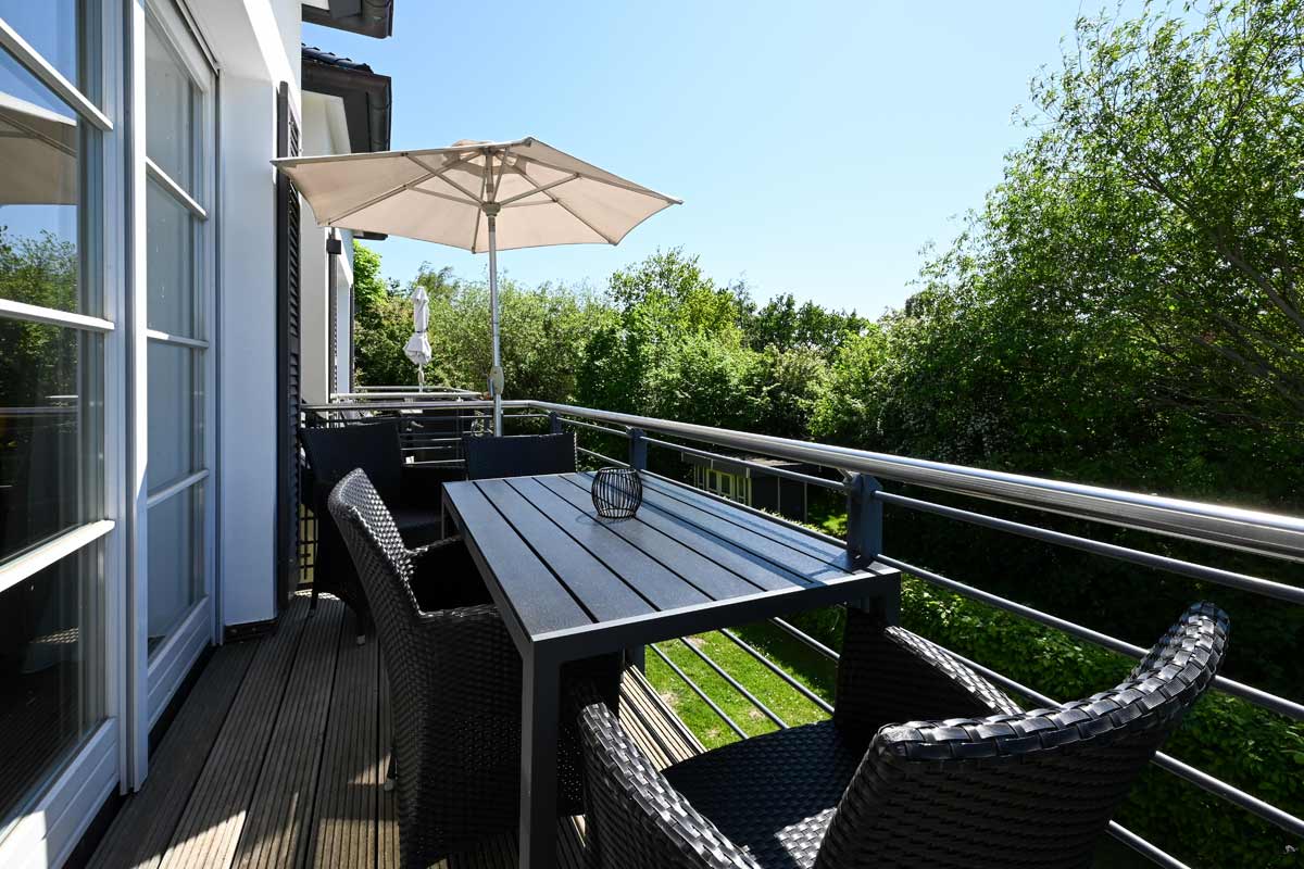 Privater Balkon der Ferienwohnung Seestern mit Sonnenschirm und ruhigem Gartenblick, Teil des Künstlerquartier Seezeichen.