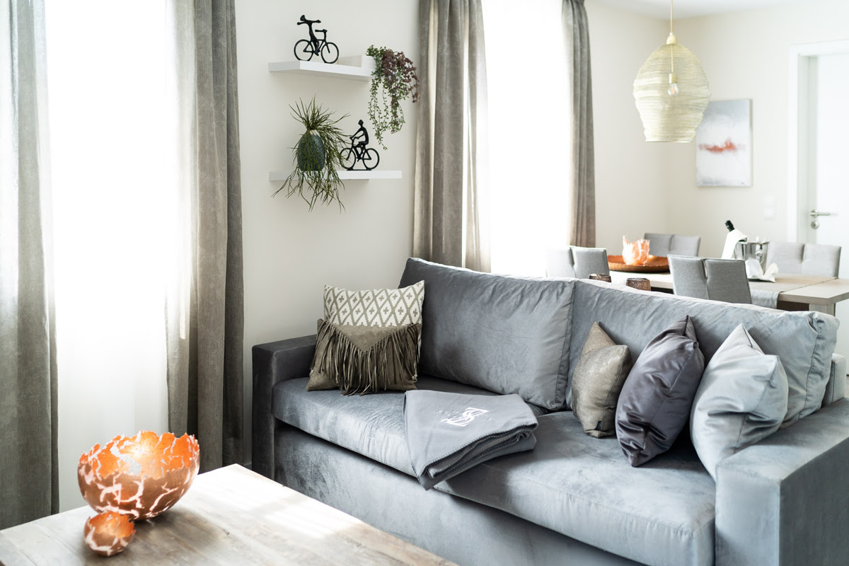 Helles Wohnzimmer mit grauem Sofa und dekorativen Kissen in der Ferienwohnung Strandoase im Hotel Künstlerquartier Seezeichen.