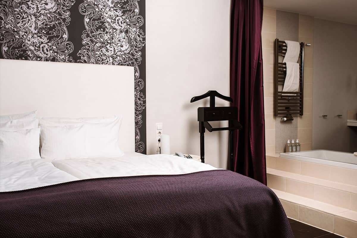 Luxurious sleeping area with access to the bathroom with bathtub of the Deluxe Suite in the Hotel Künstlerquartier Seezeichen.
